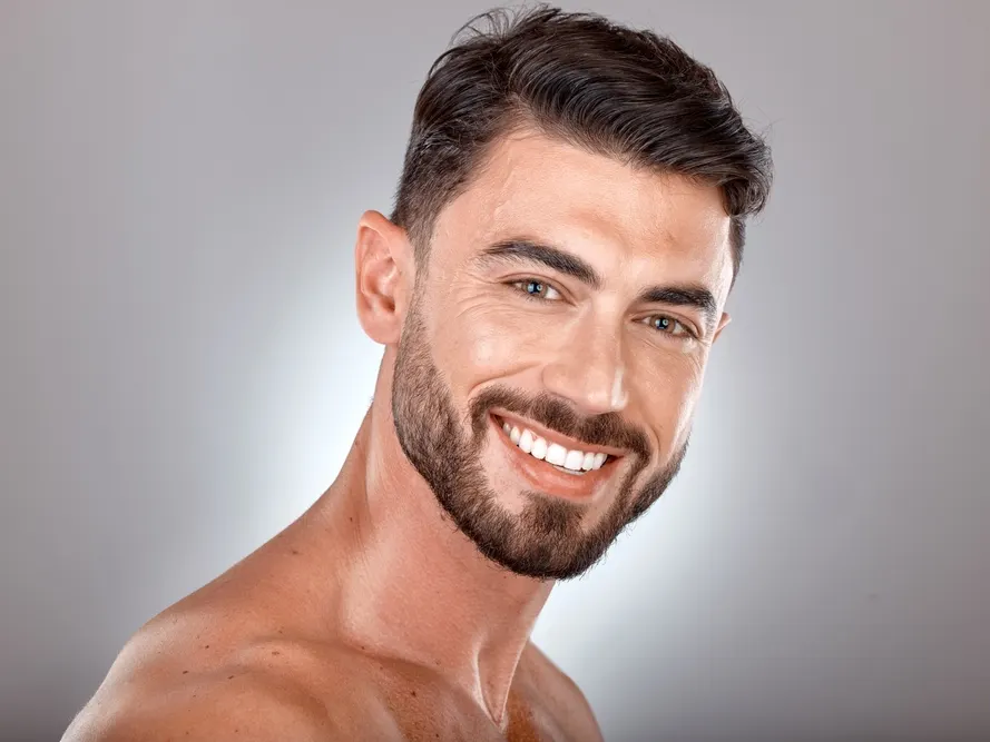 Stock photograph of a model: a smiling bearded man with clear skin against a grey background