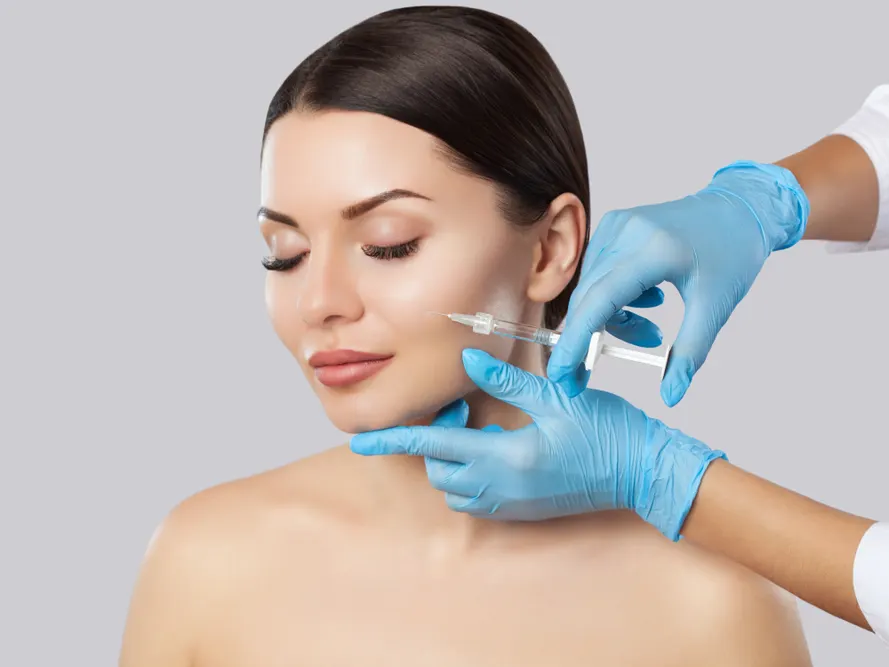 Stock photograph of a model: a woman with her eyes closed as blue-gloved hands hold a syringe near her cheek