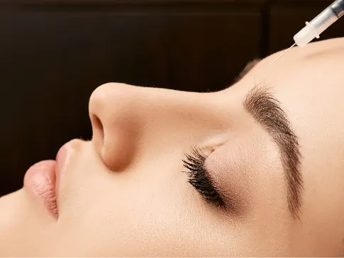 Stock photograph of a model: a purple-gloved hand holds a syringe above the forehead of a woman in profile with closed eyes