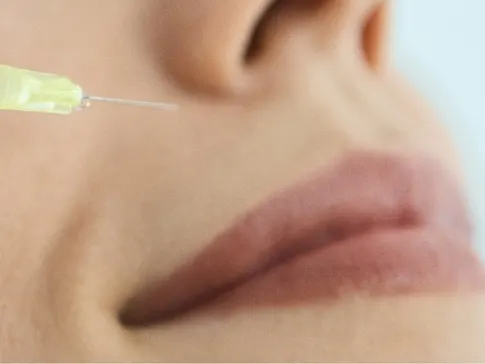 Stock photograph of a model: a syringe with a yellow-tipped needle approaches a woman's cheek beside her mouth