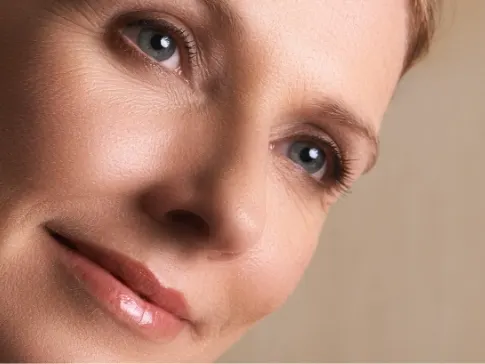 Stock photograph of a model: a woman with blue eyes tilts her head and rests a hand on her neck against a warm background