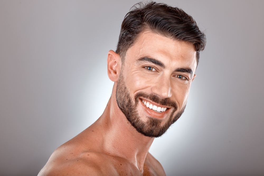 Stock photograph of a model: a smiling bearded man with clear skin against a grey background