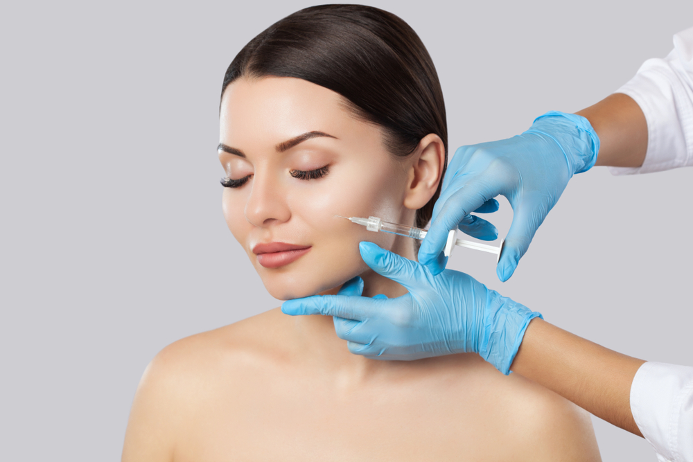 Stock photograph of a model: a woman with her eyes closed as blue-gloved hands hold a syringe near her cheek