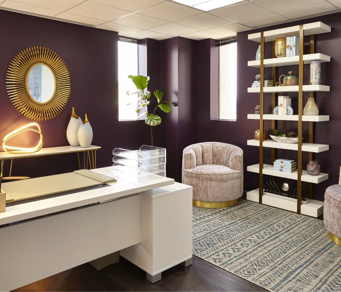 The front desk at Dermatology Specialists of Dallas: a white reception counter, a gold sunburst mirror and tall shelving against a plum wall