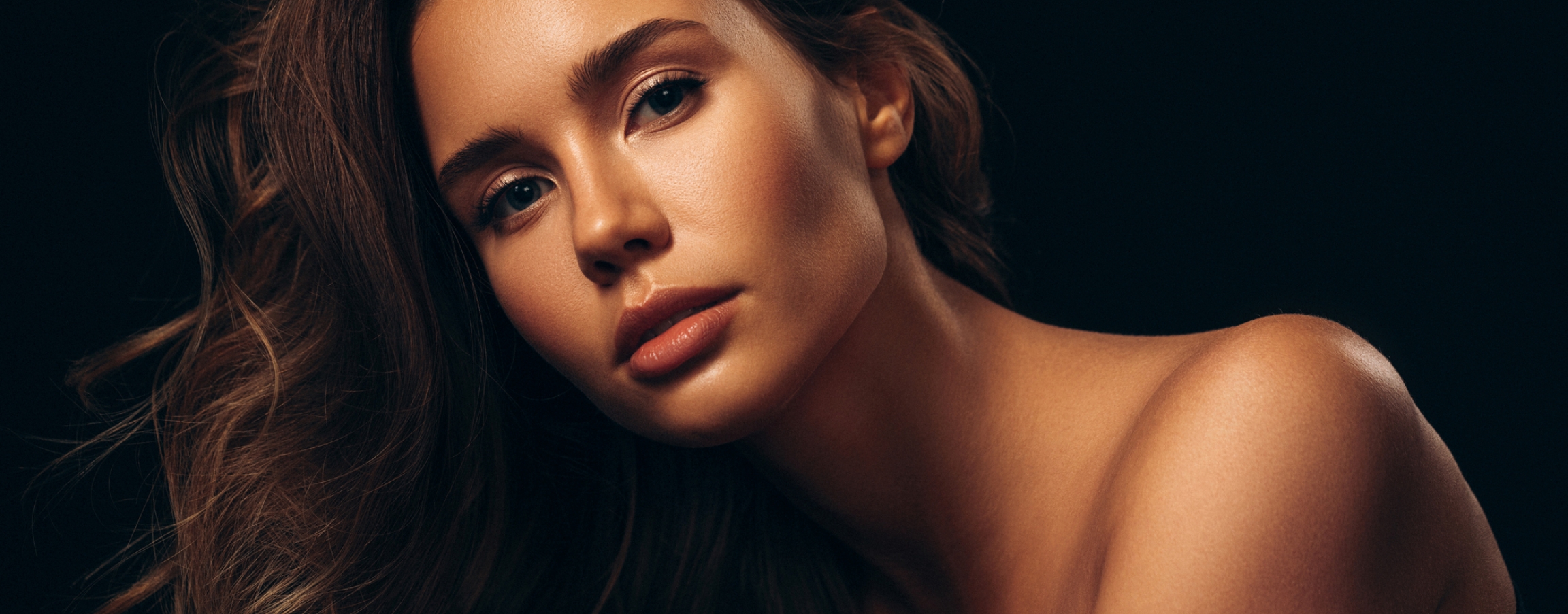 Stock photograph of a model: a woman with glowing skin and long wavy hair against a dark background