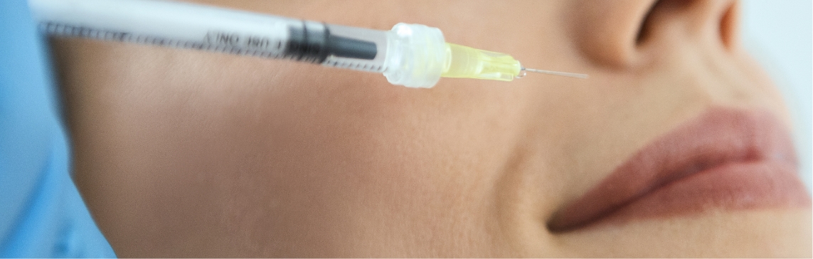 Stock photograph of a model: a syringe with a yellow-tipped needle approaches a woman's cheek beside her mouth