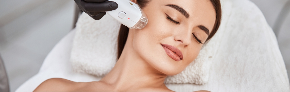 Stock photograph of a model: a woman with her eyes closed receives a treatment as a black-gloved hand holds a light handpiece to her cheek