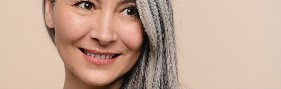 Stock photograph of a model: a smiling woman with long grey hair looks to the side against a beige background