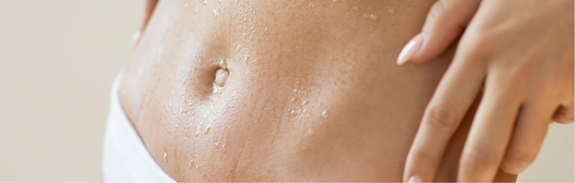Stock photograph of a model: a woman's bare abdomen with water droplets on the skin and one hand resting on her hip