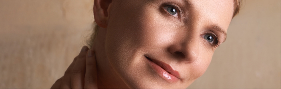 Stock photograph of a model: a woman with blue eyes tilts her head and rests a hand on her neck against a warm background